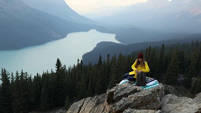 一个女人坐在山顶上，欣赏高山湖泊的美景。视频素材