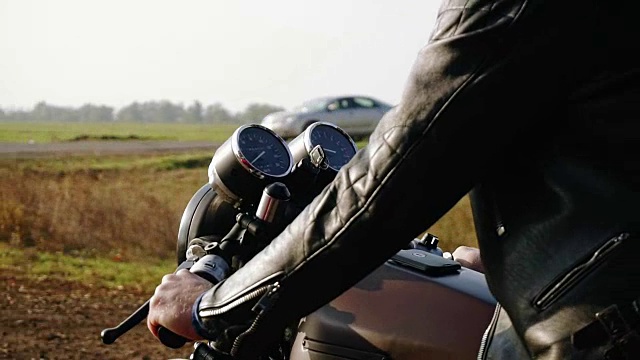 一名男子在野外的柏油路上骑着摩托车，头戴黑色头盔，身穿皮夹克。阳光灿烂的日子视频素材