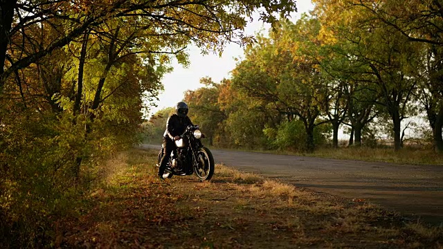 在一个阳光明媚的秋天里，一个戴着头盔、穿着皮夹克的时尚男子走到他的自行车旁，启动了引擎视频素材