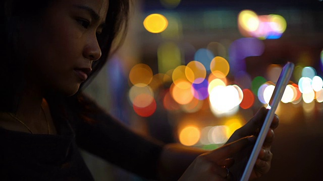 年轻的亚洲女孩使用平板电脑夜城市灯光的背景视频下载