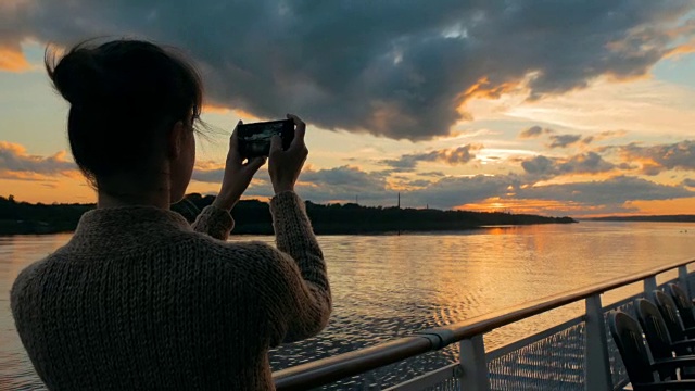 一名女子在游轮甲板上用智能手机拍摄日落剪影视频素材