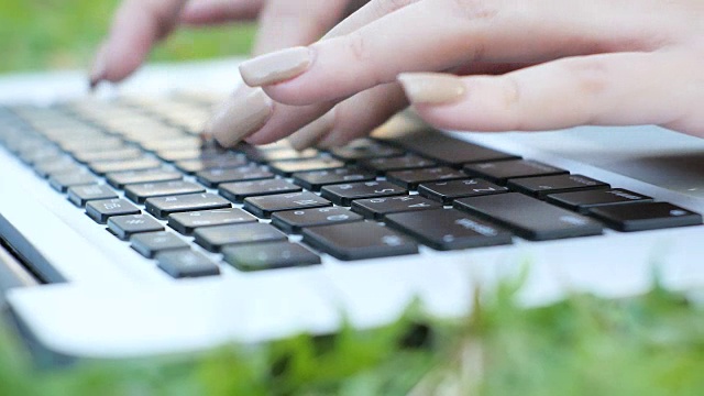 年轻的亚洲女人的腿在绿色草地上与打开的笔记本电脑。女孩的手放在键盘上。远程学习的概念。快乐的年轻亚洲潮女在公园里用笔记本电脑工作。学习在户外。视频下载