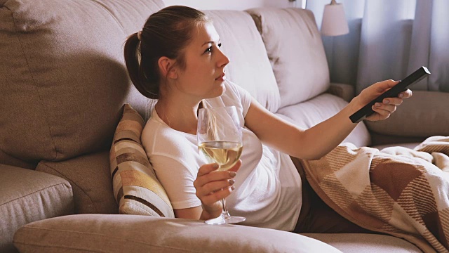 一位女士正在看电视，喝着白葡萄酒视频素材