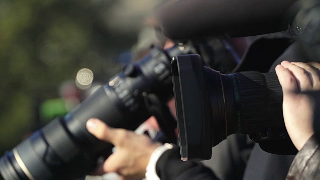 几位摄影师和摄像师用摄像机和三脚架上的长镜头在活动中记录视频和照片视频素材