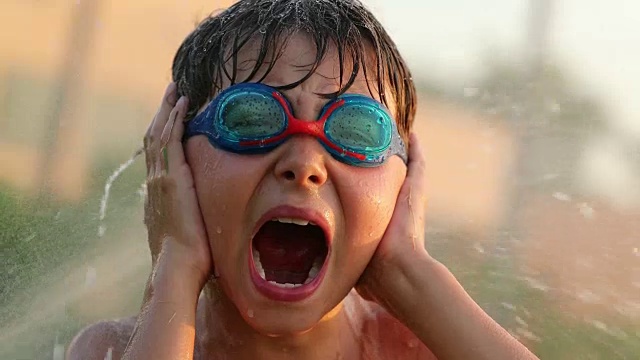 孩子尖叫着用手捂着耳朵。4k分辨率的孩子从他的肺顶部大喊，水喷洒他的水在60帧/秒的慢镜头视频素材