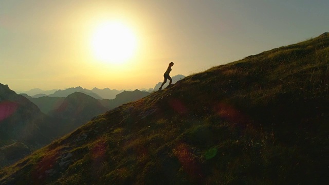 空中剪影:日落时分，一个年轻女子爬上一座山的剪影。视频素材
