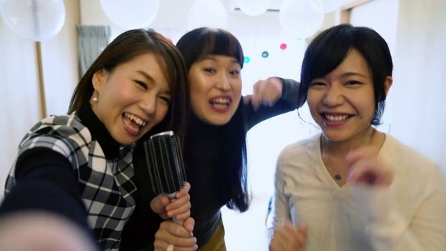 POV从一个电话作为三个年轻的日本女人在家里唱卡拉ok视频素材
