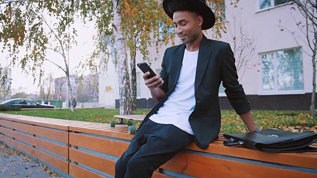 年轻的非洲黑人潮商人与长板使用智能手机在城市背景视频素材