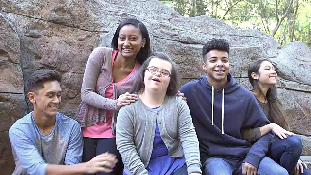 五名青少年在石墙旁的公园里，患有唐氏综合症的女孩视频素材