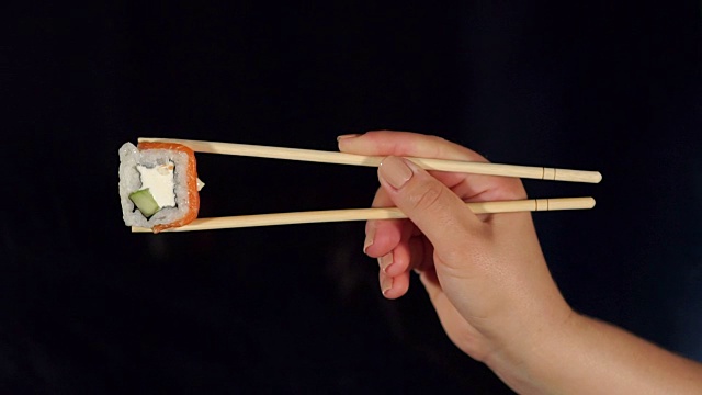 女孩拿着寿司用木筷子在黑色。视频素材