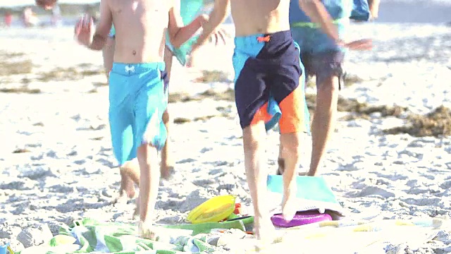 家人带着两个男孩在沙滩上，跑过来坐在沙滩上视频素材