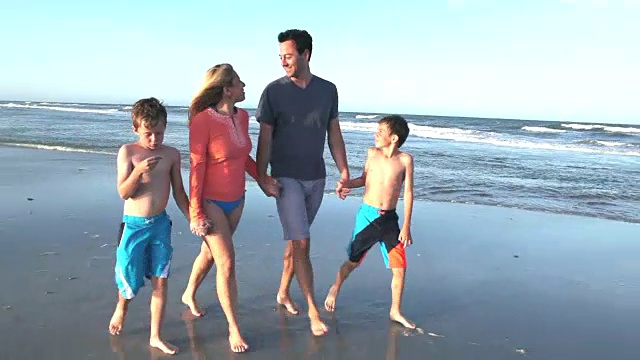 一家人和两个男孩手牵着手，在海滩上散步视频素材