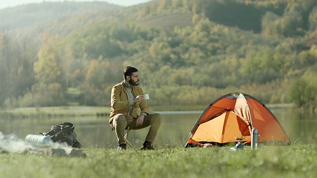 坐在湖边帐篷边喝咖啡的男人视频素材