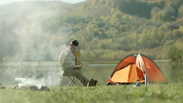 一个人坐在湖边的帐篷边看书视频素材