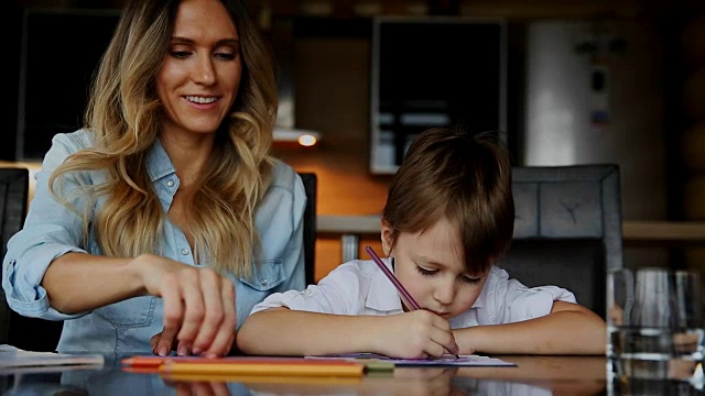 美丽的妈妈帮助她的儿子用彩色铅笔画图像。帮助发展孩子的想象力视频素材
