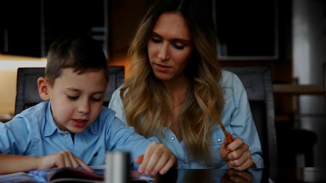 快乐的家庭，两个孩子的母亲帮助儿子做他们的家庭作业坐在厨房的大桌子视频素材