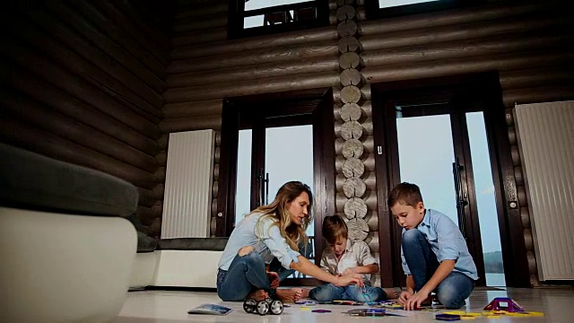 快乐的母亲和两个孩子坐在他的乡村别墅的地板上花时间一起收集儿童的设计师。带有全景窗户的客厅视频下载
