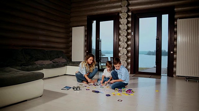 快乐的母亲和两个孩子坐在他的乡村别墅的地板上花时间一起收集儿童的设计师。带有全景窗户的客厅视频下载