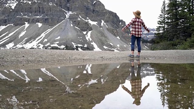 年轻女子张开双臂，站在美丽的山湖风景旁视频素材