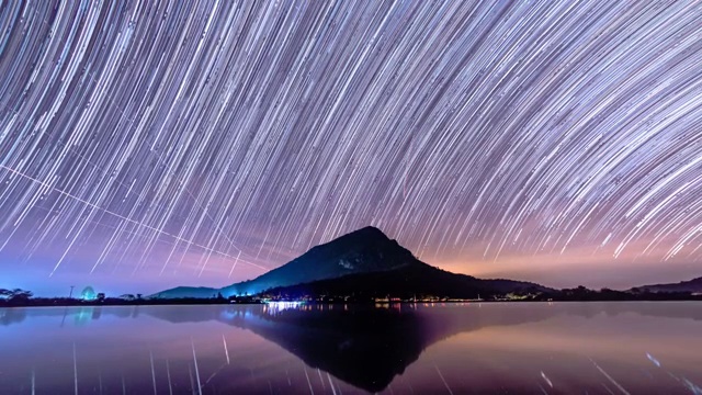 夜晚，星星的轨迹在山上和湖里移动。视频素材
