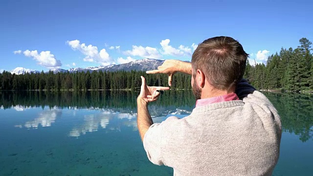 一名男子站在美丽的湖面上的木码头上，用手做了一个框架视频下载