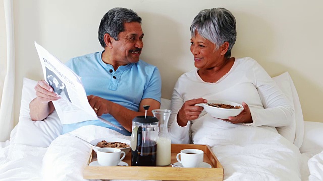 一对老年夫妇在4k卧室边吃早餐边看报纸视频素材