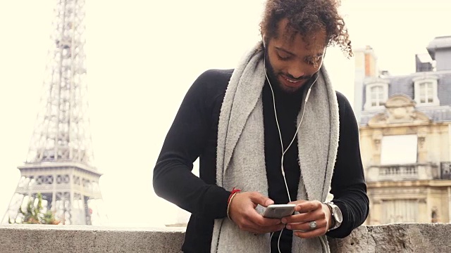 一名黑白混血男性在埃菲尔铁塔附近戴着耳机用智能手机与朋友聊天视频下载