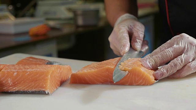 在寿司吧里，戴着手套的寿司厨师切鲜鲑鱼的特写。视频素材
