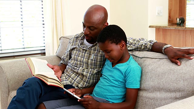 爸爸在看书，儿子在客厅用数码平板电脑4k视频素材
