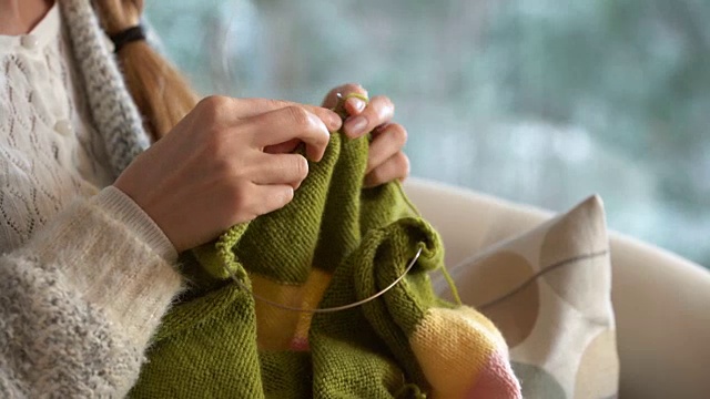 年轻女子在客厅里织着温暖的羊毛衫，窗外是雪景视频下载