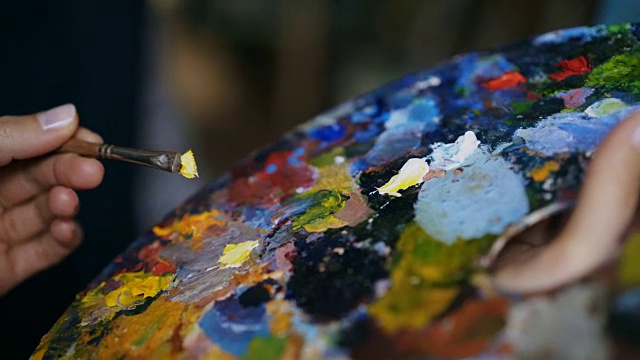 近距离跟踪拍摄的女人的手混合颜料与刷子在调色板和油画静物画在艺术家工作室视频素材