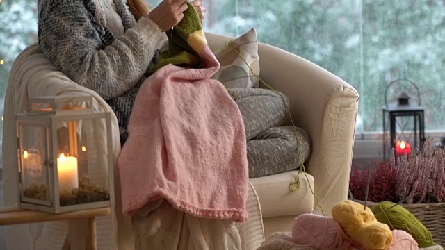 年轻女子在客厅里织着温暖的羊毛衫，窗外是雪景视频下载
