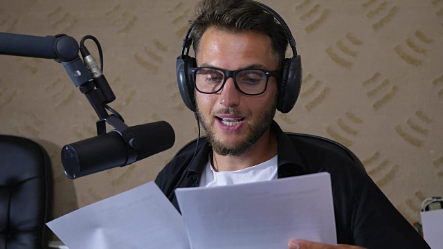 在录音室里，一个戴着眼镜的年轻人一边工作一边对着麦克风读文字视频下载
