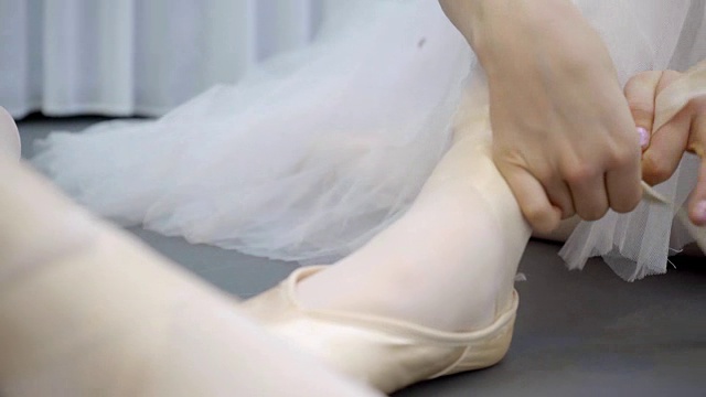 年轻的芭蕾舞女演员在芭蕾舞室把尖头鞋的带子系在腿上视频下载