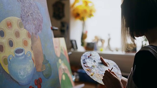 年轻的艺术家女子混合颜料与刷子在调色板和油画静物画在艺术工作室视频素材