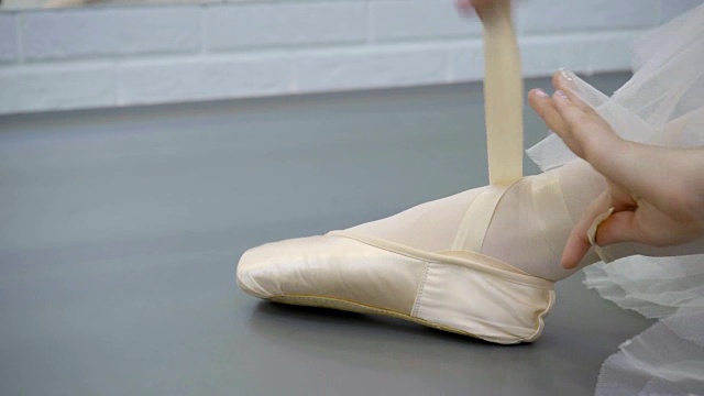 丝绸尖被绑在坐在地板上的芭蕾舞女演员的腿上视频素材