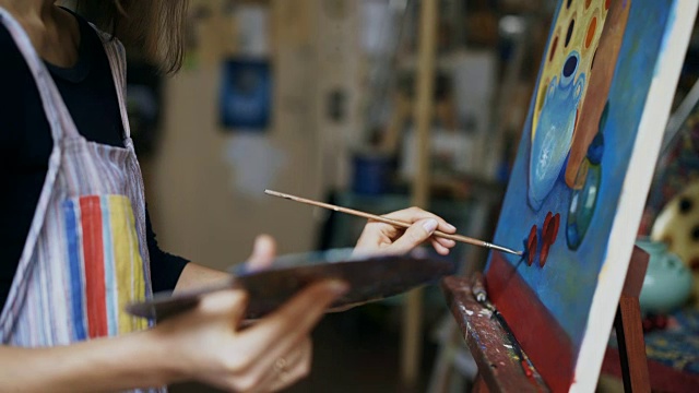 近距离跟踪拍摄的女艺术家与毛笔油画静物画在艺术工作室视频素材