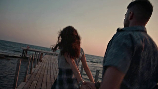 日落时分，一对年轻夫妇在木制码头上牵着手跑步视频素材