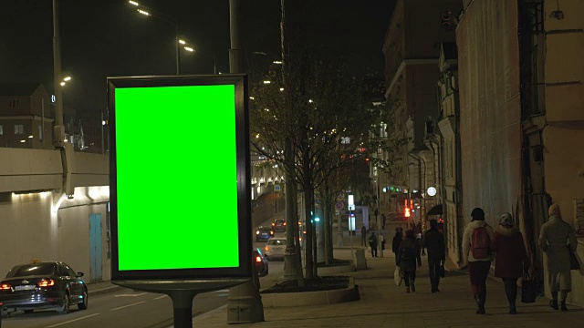 繁忙街道上的一个绿屏广告牌。人们沿着人行道走，视频素材