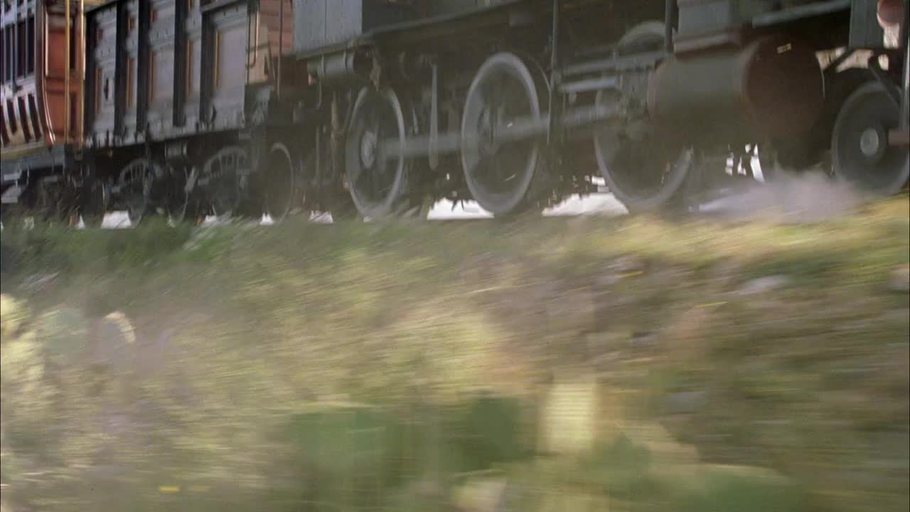 中等角度的蒸汽机火车车轮。看火车从左到右行驶。在前景看到灌木丛或灌木。火车可能经过沙漠地区。视频素材