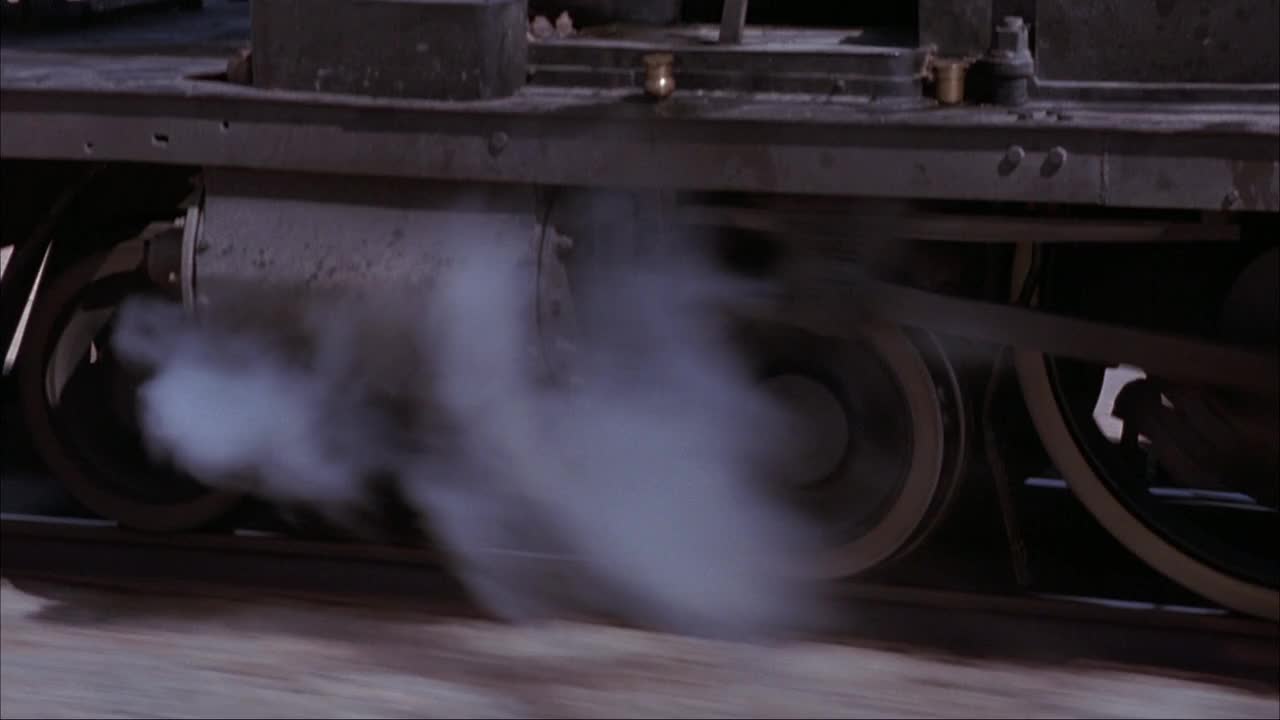 蒸汽机、火车车轮和火车轨道的中等角度。看蒸汽从火车头下面冒出来。镜头缩小到蒸汽机顶部的侧视图。参见操作列车控制器的煤和火车列车长。视频素材