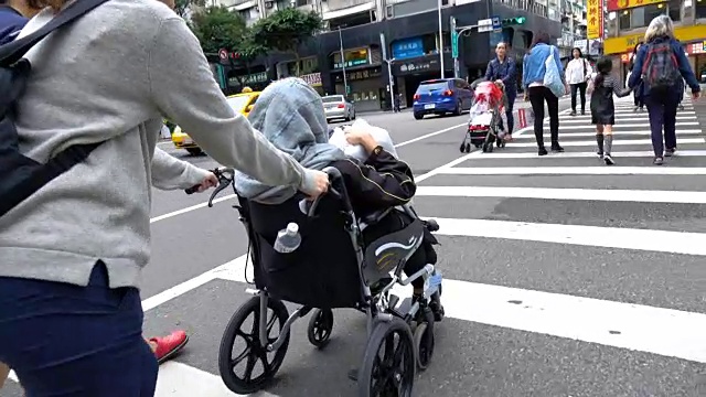 年轻女子推着轮椅上的老妇人过马路视频素材