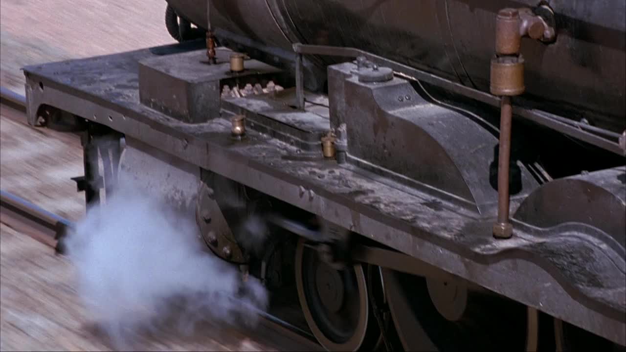 蒸汽机、火车车轮和火车轨道的中等角度。看蒸汽从火车头下面冒出来。镜头缩小到引擎顶部。参见操作列车控制器的煤和火车列车长。看火车从右到左穿越沙漠景观。视频素材