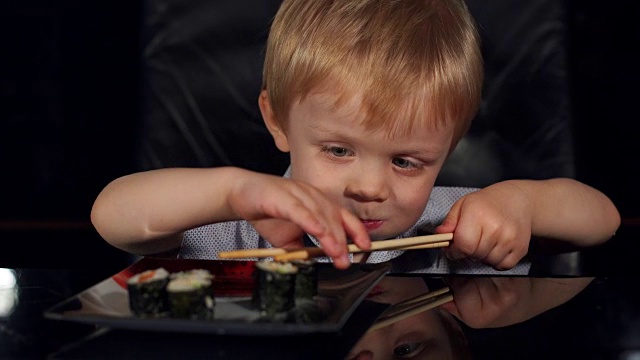 可爱的小男孩用木筷子吃寿司。视频素材
