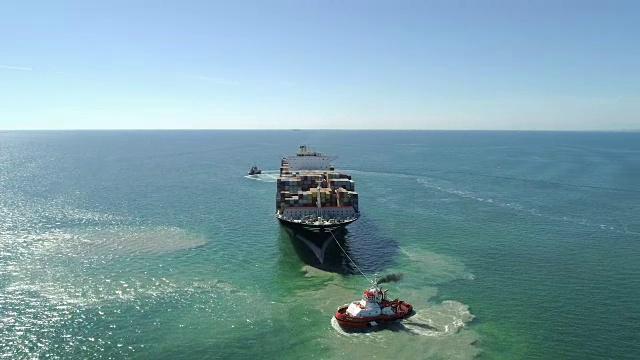 航拍:小型船只跟随大型集装箱船前往海港。视频下载