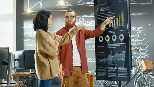 女性开发人员和男性统计人员使用交互式白板演示触摸屏查看图表、图表和增长统计数据。他们在时尚创意办公室工作。视频素材