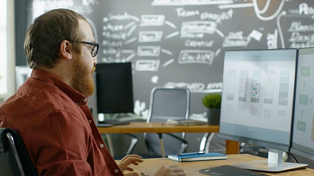 男性手机游戏开发人员在个人电脑上工作，设计线框，他在思考手势抚平胡须。他就职于创意独立工作室。视频素材
