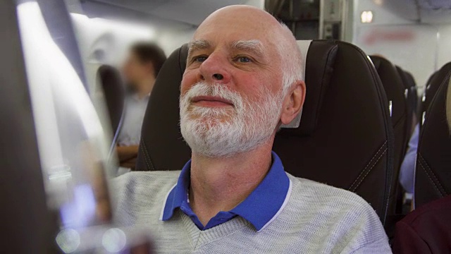 老人白天在飞机上飞行。因时差而疲惫的男性在乱流中靠近窗户放松视频素材
