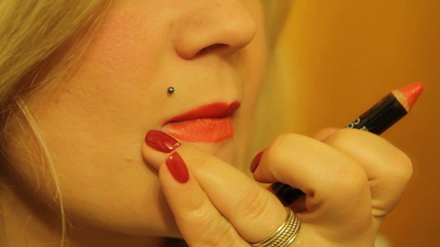 年轻漂亮的金发女人在镜子前涂着她的嘴唇鲜红色的口红视频素材