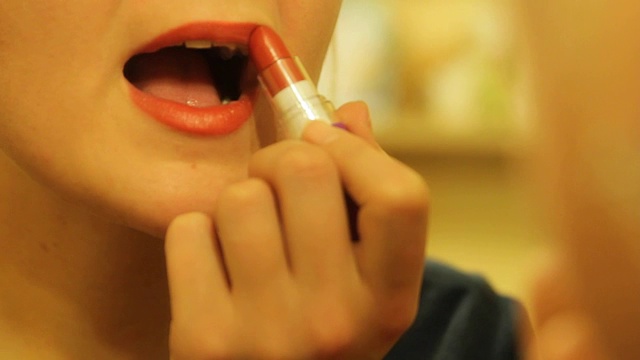 年轻漂亮的金发女人在镜子前涂着她的嘴唇鲜红色的口红视频素材